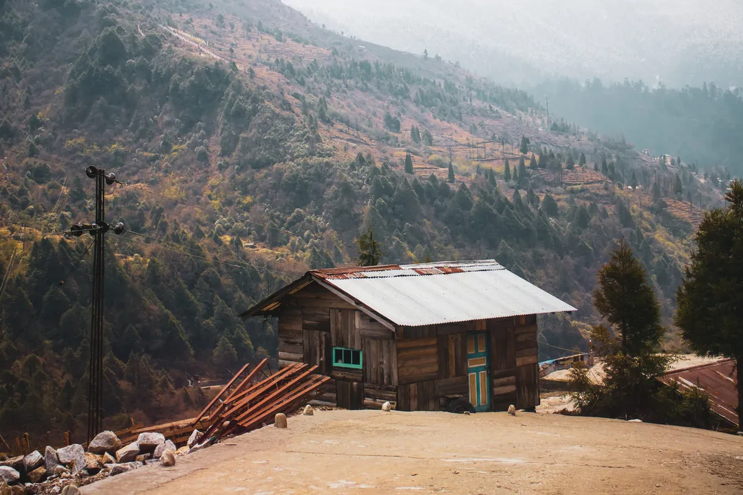 Weathered wooden house with a tin roof on a forested Himalayan hillside
