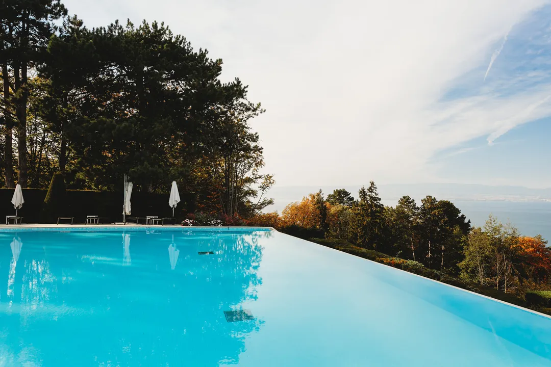 Infinity pool with parasols at the edge of a hillside, pine trees and a wide valley view