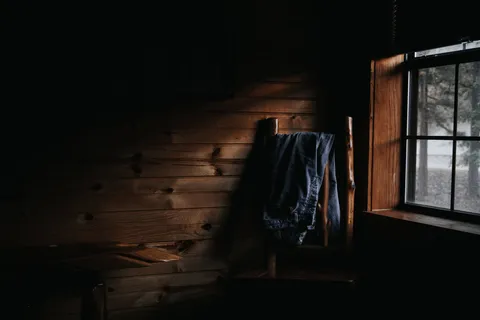 Dim wooden room with plank walls, a jacket on a peg and light from a small window